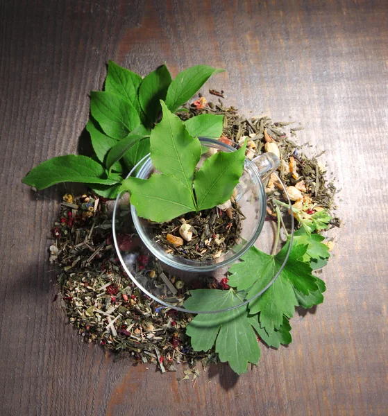 Coupe en verre avec des fleurs et des herbes sèches, des ingrédients de fruits pour le thé, sur fond en bois de couleur — Photo