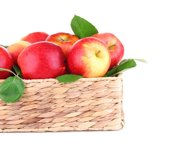 Rijpe zoete appels met bladeren in rieten krat, geïsoleerd op wit — Stockfoto