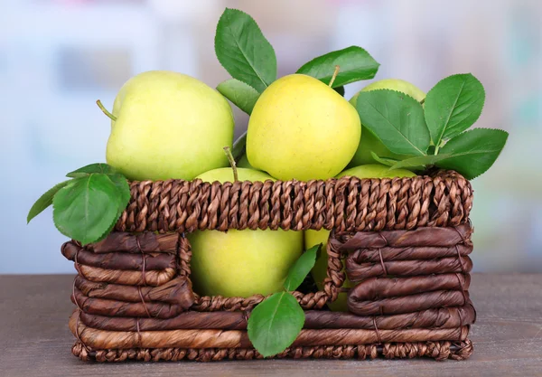 Rijpe zoete appels met bladeren in rieten krat op lichte achtergrond — Stockfoto