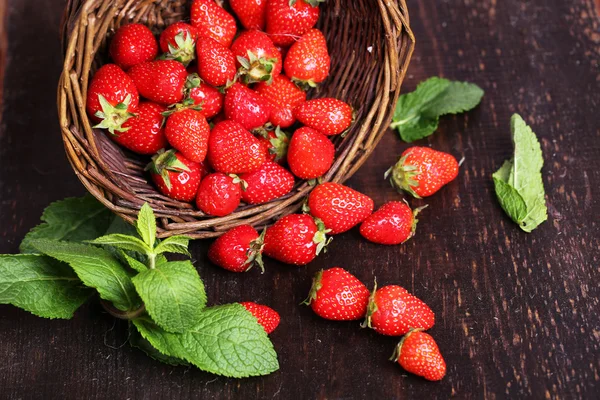 Mogna söta jordgubbar i rotting korg på trä bakgrund — Stockfoto