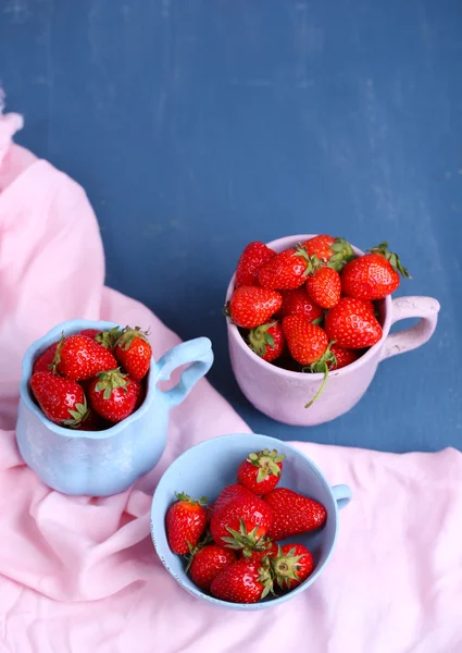 Ripe sweet strawberries in mugs  on color wooden background — Stock Photo, Image