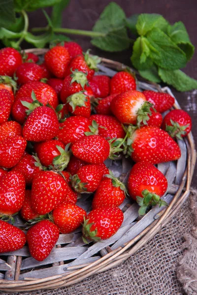 Maturare dolci fragole su stuoia di vimini, su sfondo di legno a colori — Foto Stock