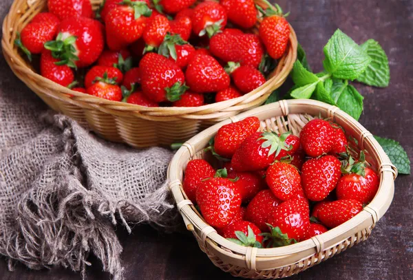 Rijp zoete aardbeien in rieten mand en muntblaadjes op houten ondergrond — Stockfoto