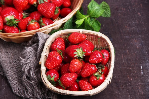 Reife süße Erdbeeren im Weidenkorb und Minzblätter auf Holzgrund — Stockfoto