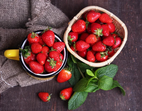 Fraises douces mûres dans un panier en osier et feuilles de menthe sur fond de bois — Photo