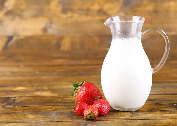 Reife süße Erdbeeren und Krug mit Milch auf farbigem Holzhintergrund — Stockfoto