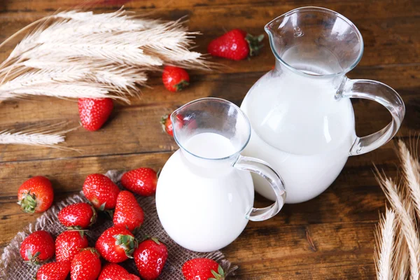 Reife süße Erdbeeren und Krug mit Milch auf farbigem Holzhintergrund — Stockfoto
