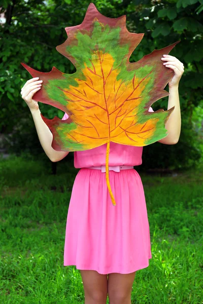 Girl holding decorative maple leaf in park — Stock Photo, Image