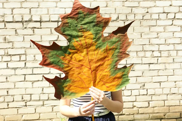 Girl holding decorative maple leaf on wall background — Stock Photo, Image