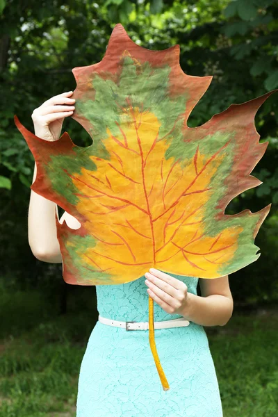 Girl holding decorative maple leaf in park — Stock Photo, Image