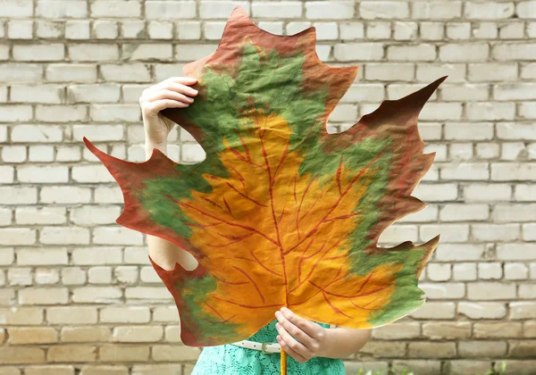 Girl holding decorative maple leaf on wall background — Stock Photo, Image