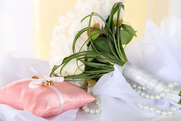 Schöner Hochzeitsstrauß und dekoratives Kissen für Trauringe auf Tisch auf hellem Hintergrund — Stockfoto