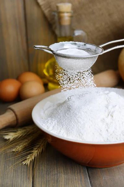 Sifting flour into bowl on table on wooden background — Stock Photo, Image