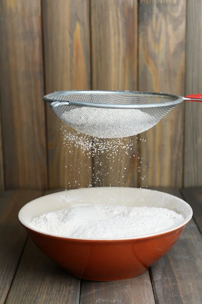 Sifting flour into bowl on table on wooden background — Stock Photo, Image