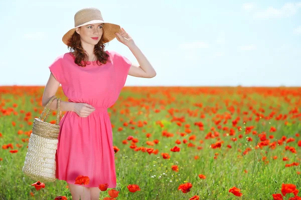 Beautiful young woman holding wicker bag in poppy field — Stock Photo, Image