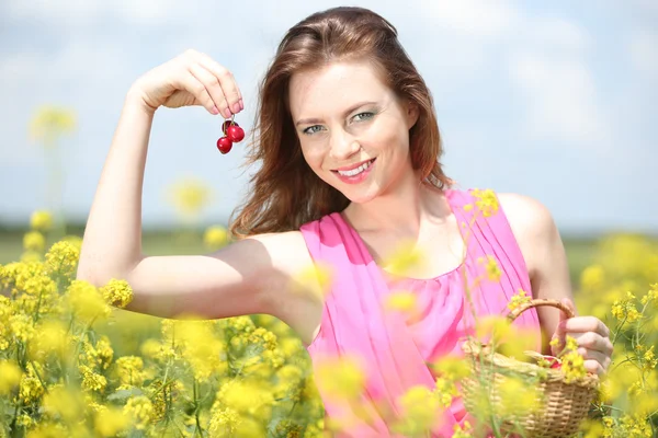 Hermosa joven mujer sosteniendo canasta de mimbre con cerezas en el campo — Foto de Stock