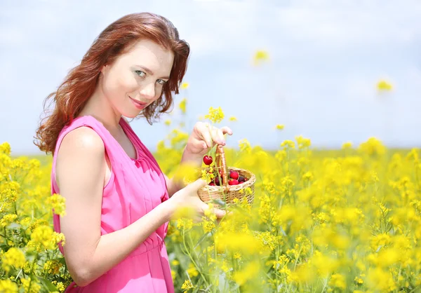 Vacker ung kvinna håller rotting korg med körsbär i fältet — Stockfoto