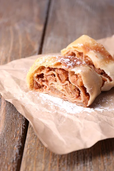 Gustoso strudel di mele fatto in casa su tovagliolo di carta, su sfondo di legno — Foto Stock