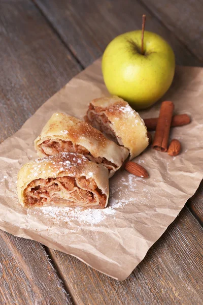 Sabroso strudel de manzana casero en servilleta de papel, sobre fondo de madera —  Fotos de Stock