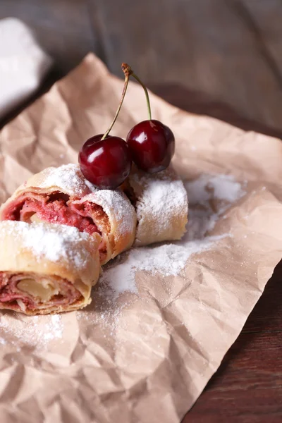 Gustoso strudel fatto in casa e dolce ciliegia fresca su tovagliolo di carta, su sfondo tavolo di legno — Foto Stock