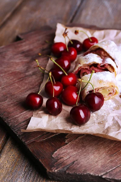 Strudel maison savoureux et cerise douce fraîche sur une serviette en papier, sur fond de table en bois — Photo