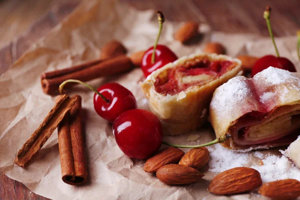 Leckerer hausgemachter Strudel und frische Süßkirsche auf Papierserviette, auf Holztischhintergrund — Stockfoto