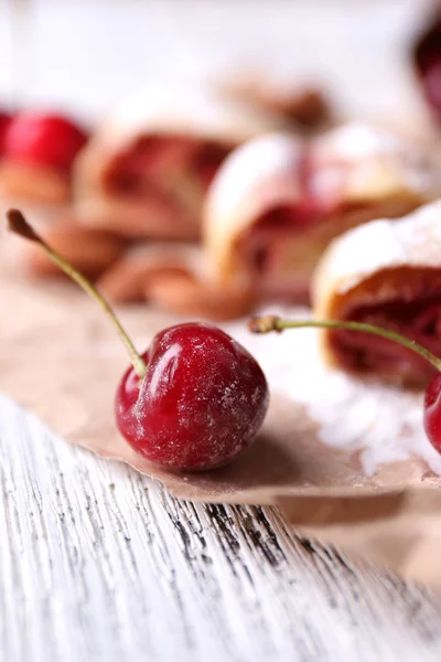 Saboroso strudel caseiro e cereja doce fresca no guardanapo de papel, no fundo da mesa de madeira — Fotografia de Stock