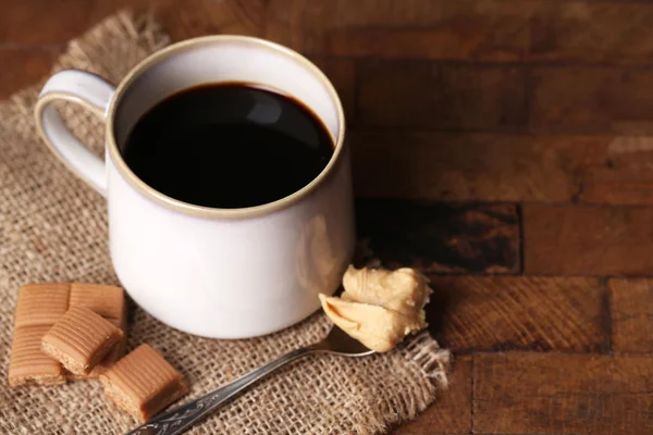 Taza con café caliente en servilleta de saco, sobre fondo de mesa de madera — Foto de Stock