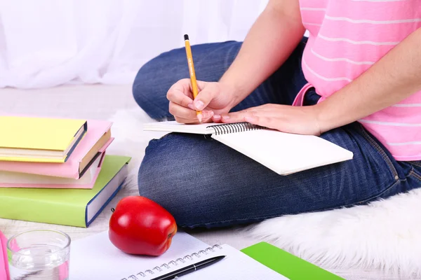 Closeup of young female student sitting on floor and studying, on light background — Stock Photo, Image