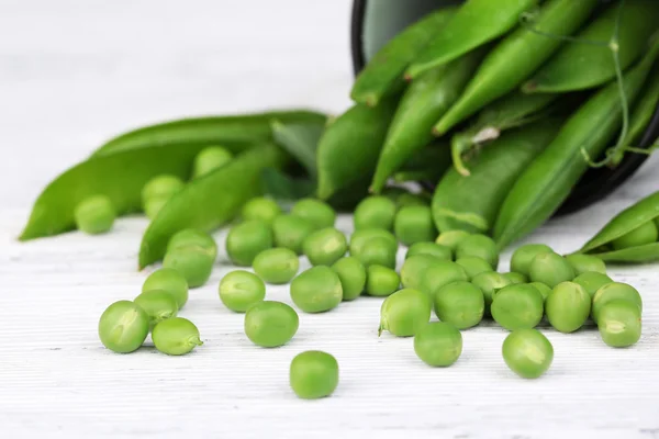 Fresh green peas in metal cup on wooden table — Stock Photo, Image