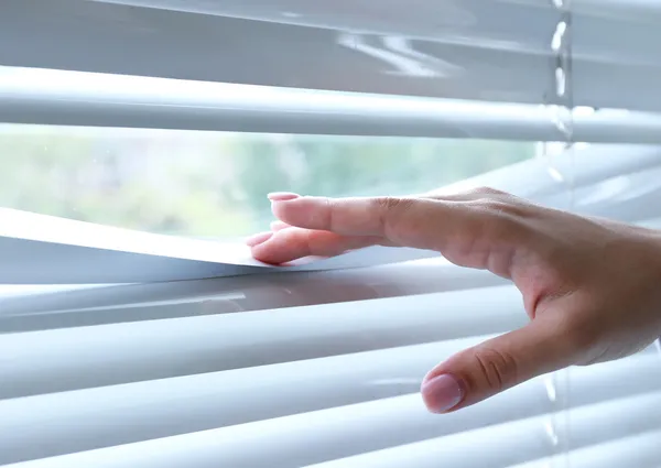 Kvinnliga händer som skiljer lameller av persienner med ett finger för att se igenom — Stockfoto