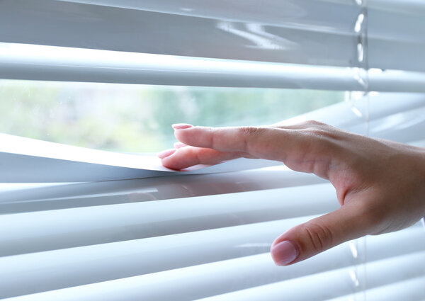 Female hand separating slats of venetian blinds with a finger to see through