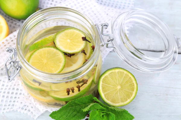 Pickled limes and cloves in glass jar, on color wooden background — Stock Photo, Image