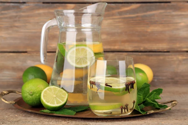 Fresh summer drink with lime and cloves in glass and jug, on color wooden background — Stock Photo, Image