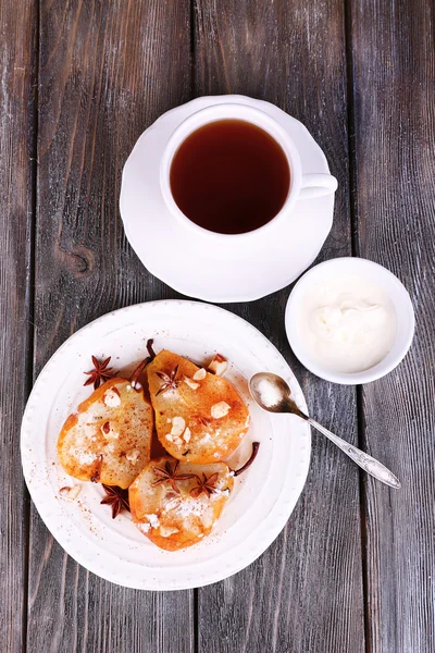 Poires cuites au four avec sirop sur plaque, bol avec crème et tasse de thé sur fond en bois de couleur — Photo