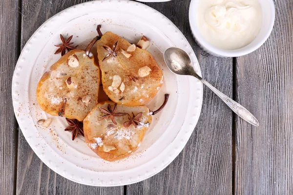 Baked pears with syrup on plate, bowl with cream and cup of tea on color wooden background — Stock Photo, Image