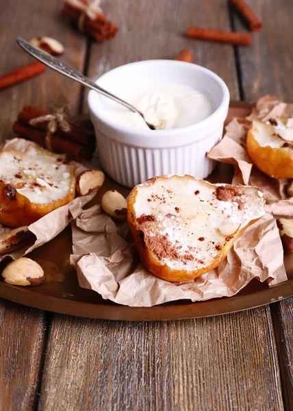 Pere al forno con sciroppo su piatto, ciotola con crema su vassoio, su sfondo di legno a colori — Foto Stock