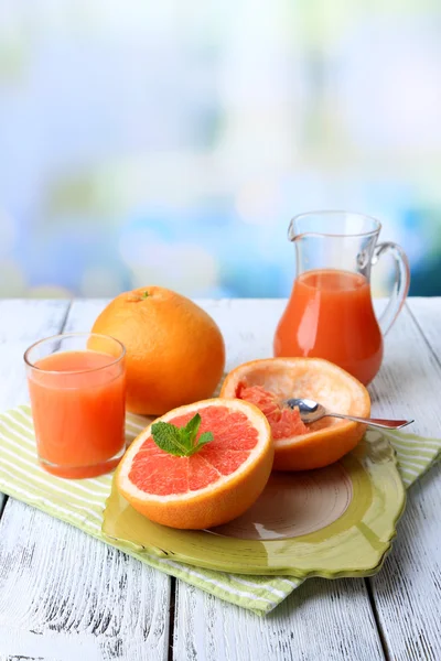 Half of grapefruit, glass jug with fresh juice and spoon on plate on light background — Stock Photo, Image