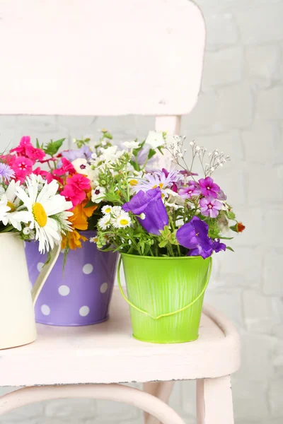 Boeket van kleurrijke bloemen in decoratieve emmers, op stoel, op lichte muur achtergrond — Stockfoto