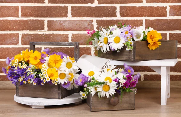 Schöne Blumen in Kisten auf Holzständer auf Backsteinmauer Hintergrund — Stockfoto