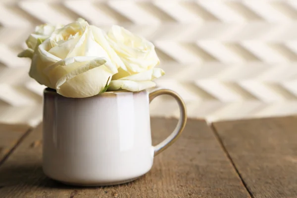 Rosas brancas bonitas na xícara na mesa de madeira — Fotografia de Stock