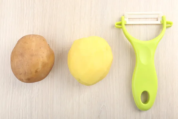 Éplucheur et pommes de terre sur table en bois — Photo