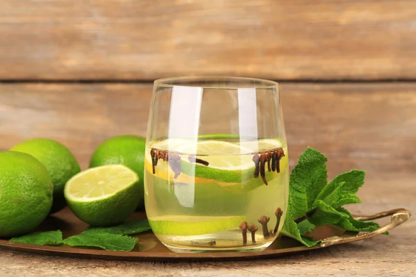 Bevanda estiva fresca con lime e chiodi di garofano in vetro, su sfondo di legno a colori — Foto Stock