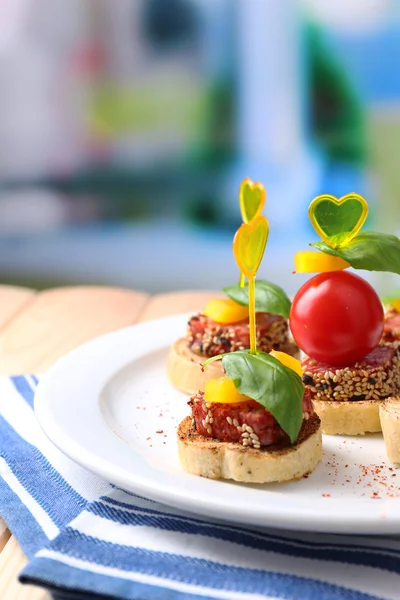 Smakelijke canapeetjes met salami, tomaat, peper en basilicum bladeren, op plaat, op houten tafel, op lichte achtergrond — Stockfoto