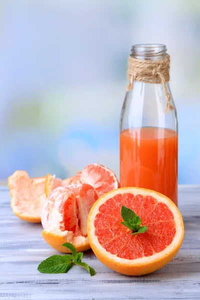 Pomelos pelados maduros y jugo fresco en la mesa de madera de color, sobre fondo brillante — Foto de Stock