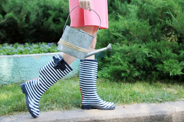 Jeune femme en bottes en caoutchouc tenant arrosoir, en plein air — Photo