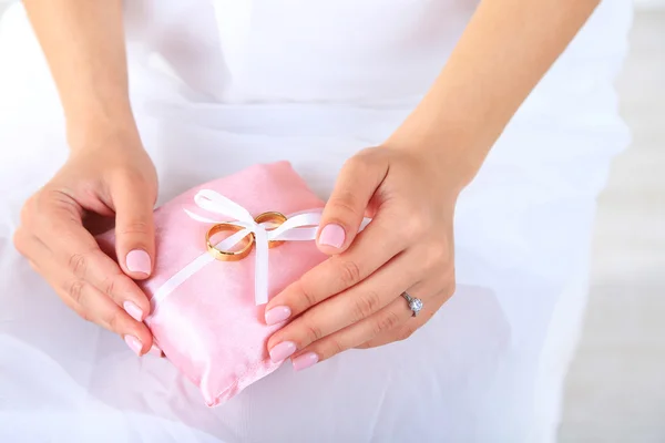 Bruid in witte jurk en handschoenen houden decoratieve kussen met bruiloft ringen, close-up, op lichte achtergrond — Stockfoto