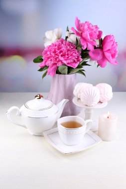 Cam vazo içinde sunulan güzel peonies, çay Kupası ve hatmi, masada açık renkli üzerinde kompozisyon
