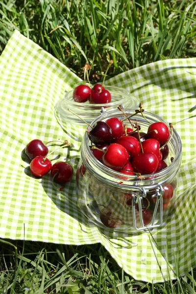 Doces cerejas maduras em frasco de vidro, em guardanapo, em fundo de grama verde — Fotografia de Stock