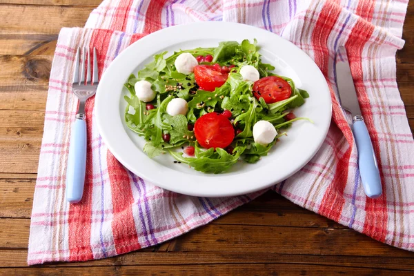 Green salad made with  arugula, tomatoes, cheese mozzarella balls and sesame  on plate, on wooden background — Stock Photo, Image